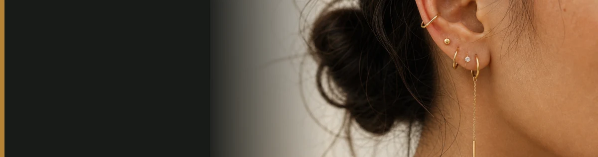 An editorial close-up of delicate gold ear jewelry fading into warm charcoal and ivory
